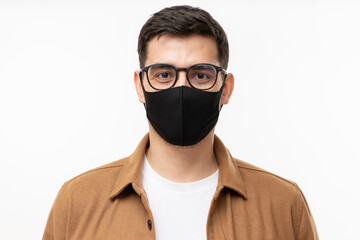 Portrait of young man wearing trendy brown cargo shirt, glasses and black face mask standing isolated on gray background