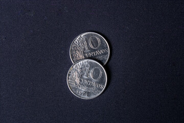 Two overlapping old ten-cent coins dated 1974 used in Brazil on a dark black background with light positioned from left to right.