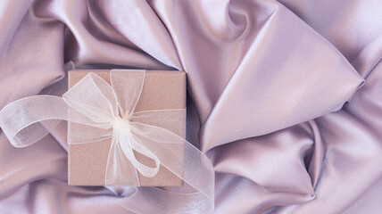 Elegant gift box on drapery of violet satin. Abstract luxury and romantic background. Minimal female concept.
