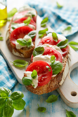 Caprese sandwich based on sourdough bread with the addition of tomatoes, mozzarella cheese, fresh basil and olive oil on a white board close up view