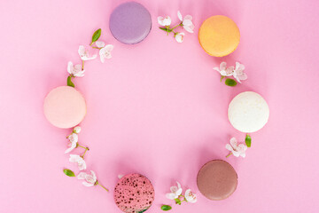 Circle of colourful french macarons and spring blossoms on pink pastel background. Romantic, minimal composition.