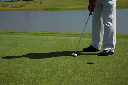 Detalhe de taco de golf, as pernas do golfista e a bola, gramado e o buraco. Esporte ao ar livre. - Powered by Adobe