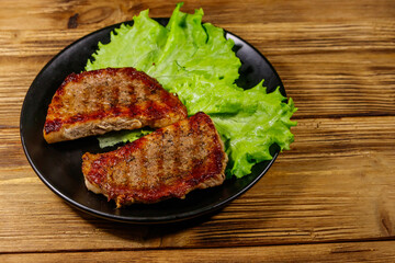 Grilled pork steaks with lettuce leaves on wooden table