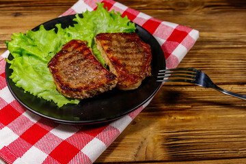 Grilled pork steaks with lettuce leaves on wooden table