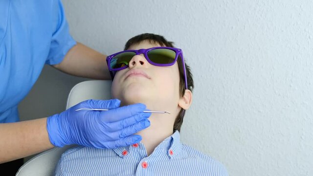 doctor examines oral cavity of small patient, molars grow, length of frenum of the tongue, boy, kid with open mouth, close up of child&rsquo;s teeth