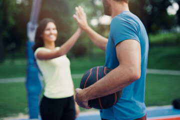 Beautiful young couple enjoying together and playing on basketball court. Bright sunny summer day..