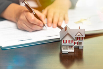 Man signing real estate contract papers with small model home in front.