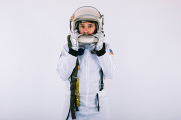 Male cosmonaut in space suit and helmet, holding helmet with hands, on white background.