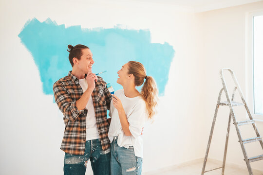 Happy couple painting new apartment walls in blue color together.