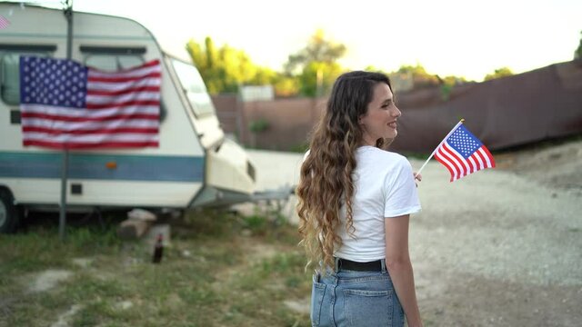 Chica joven con top blanco y bandera de estados unidos frente a una caravana 