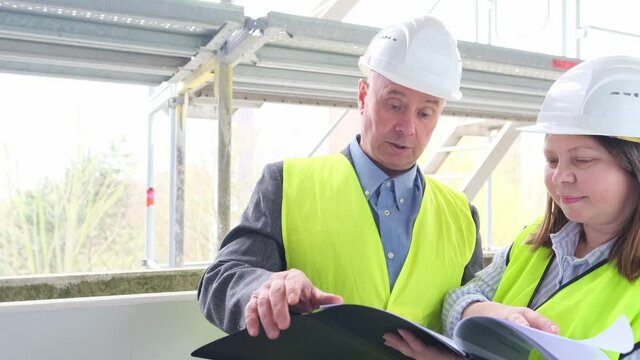experienced elderly architect, female engineer constructor in protection of white helmet accept the object, sign documents at construction site, concept of civil engineering, cooperation