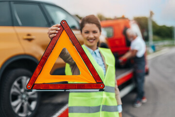 Middle age business woman after car accident putting safety or warning foldable triangle on the road. Help on the road concept..