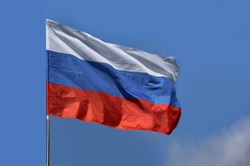 photo of the beautiful colored national flag of the modern state of Russia waving against a blue sky, textured fabric, concept of tourism, emigration, economics and politics, closeup