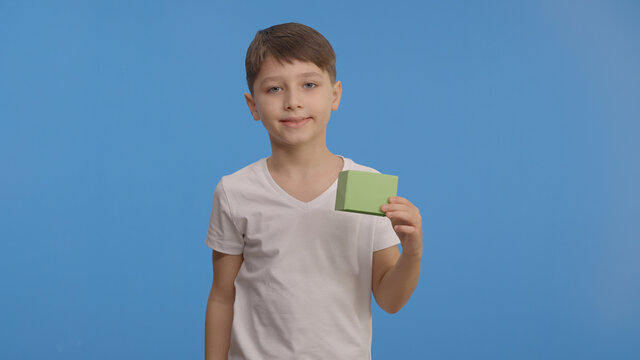 Beautiful little boy is holding a green box in his hand and pointing to the box. Creative people can replace the green box with whatever and product they want. Blue background.