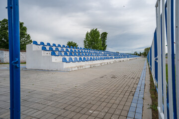 Empty grandstand with blue seats with no people on small stadium in cloudy day
