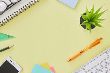 Top View or Flat Lay Modern Office Desk or Office Table with Stationery as Keyboard,Pen,Stick Note,Mobile Phone,Pencil,Ruler,Notebook,Glasses,Office Plants. Yellow Minimalist Workspace Background