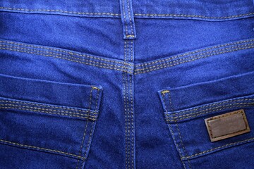 Fototapeta premium The texture of modern blue denim cloth. Dark jeans background with thin seams and a large pocket.