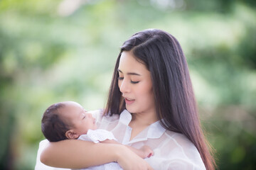 A healthy Asian woman mother, raising a baby in a green garden atmosphere, having a good environment, giving love and warmth.