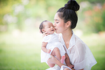 A healthy Asian woman mother, raising a baby in a green garden atmosphere, having a good environment, giving love and warmth.