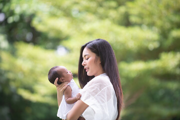 A healthy Asian woman mother, raising a baby in a green garden atmosphere, having a good environment, giving love and warmth.