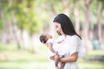 A healthy Asian woman mother, raising a baby in a green garden atmosphere, having a good environment, giving love and warmth.