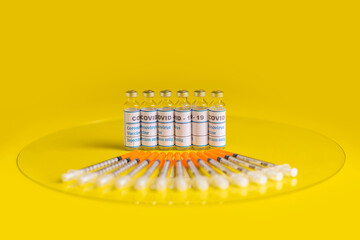Envases de vacuna contra el covid-19 con jeringas en un fondo amarillo 