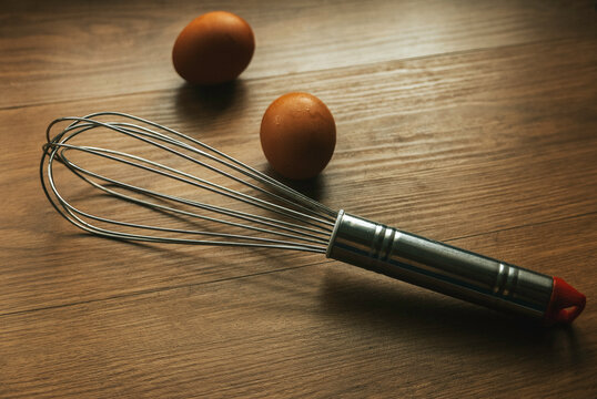 Stainless Steel of whisk and an egg on wooden background.