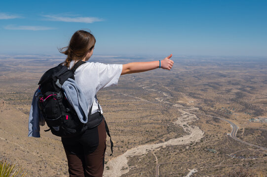 the young girl standing from  the hill hitchhiking over the background of the  desert road