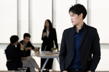 A tomboy woman in casual suit standing with self-confident in office and colleagues in background. Transgender in modern business workplace concept