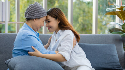 Older Asian woman patient covered the head with clothes effect from chemo treatment in cancer cure process touch her daughter's forehead with happy