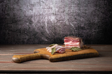 Appetizer on a cutting board, sliced lard, with bay leaf, on a wooden countertop, on a gray background