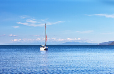 Baikal Lake in summer. Minimalistic landscape with sailing yacht in Barguzinsky Bay on sunny day against backdrop of mountains of Svyatoy Nos peninsula. Natural background. Summer travel and cruises