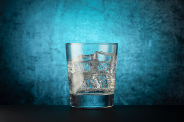glass glass with mineral water with ice, on a dark background with a light spot in the center