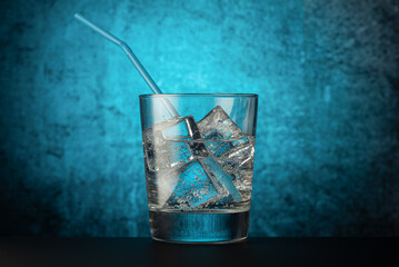 glass glass with mineral water with ice, and a drinking tube, on a dark background with a light spot in the center