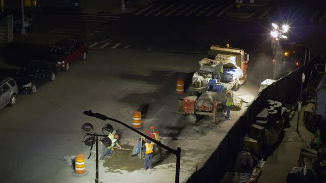 A construction crew mixing cement for road repair late at night in the city.