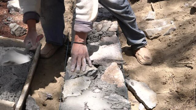 single mexican construction worker building a small stone wall with rocks and concrete. Close up top shot