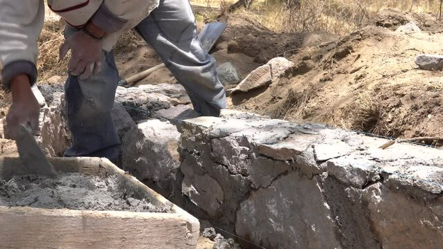 Humble mexican construction worker building a small stone wall with rocks and concrete. Close up horizontal shot