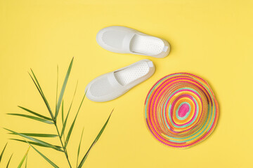 A multicolored hat, white sneakers under the leaves of a palm tree on a yellow background.