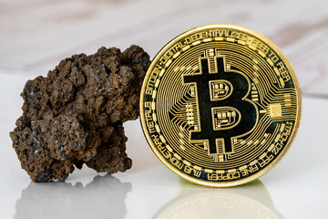 Pièce en or avec le logo de Bitcoin sur une surface blanche avec une roche représentant le minage...