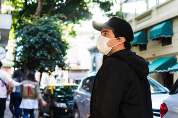 young tourist walking through the streets of San telmo Buenos Aires, at sunset. wearing a surgical face mask, a cap and a black jacket.