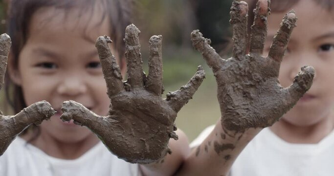 Two asian child girls playing mud and showing dirty hands after planting the tree in the garden together with fun.Concept of child love in environmental conservation.Slow motion shot.
