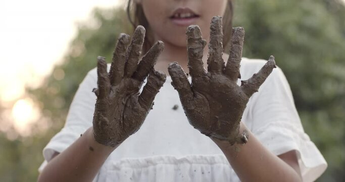 Asian child girl playing mud and showing dirty hands after planting the tree in the garden.Concept of child love in environmental conservation.Slow motion shot.