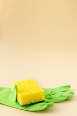 Yellow dishwashing sponge and green rubber gloves on neutral beige background, cleaning concept
