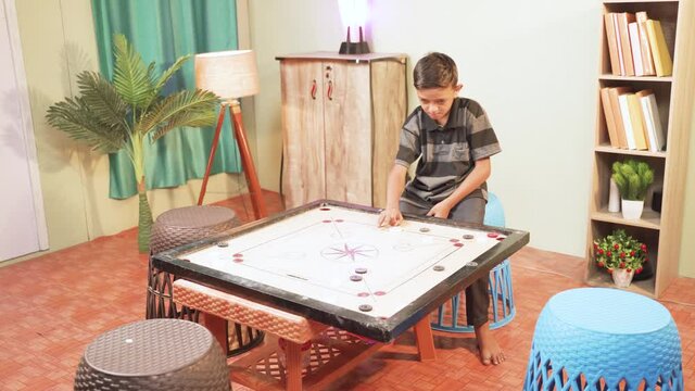 Alone kid playing carrom by changing places - concept of Child practicing game or teenager playing single at home due to coronavirus covid-19 lockdown.