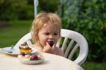 Baby eating cake. Feeding kids. Child eating fruit in the garden outside in summer.