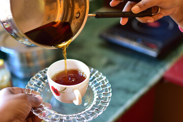 Young woman using kettle for make tea or black coffee on kitchen at room interior background.Women's hands pour water from a teapot into a cup. Blurred, flares effect
