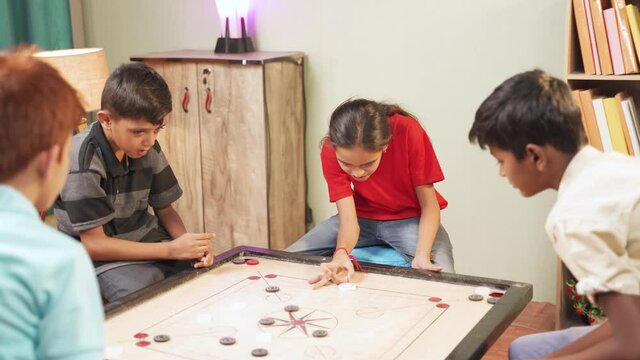 Intelligent pro teenager girl trying to hit all coins while playing carrom board with her friends or siblings at home - concept of prodigy kid