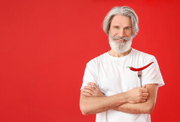 Senior man with chili pepper on color background