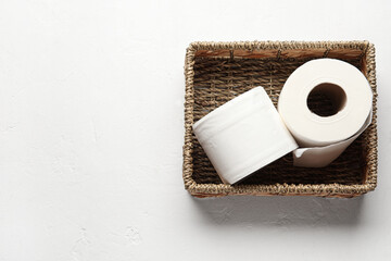 Wicker basket with rolls of toilet paper on white background