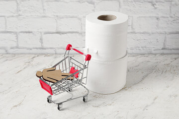 Creative composition with rolls of toilet paper and shopping cart near brick wall